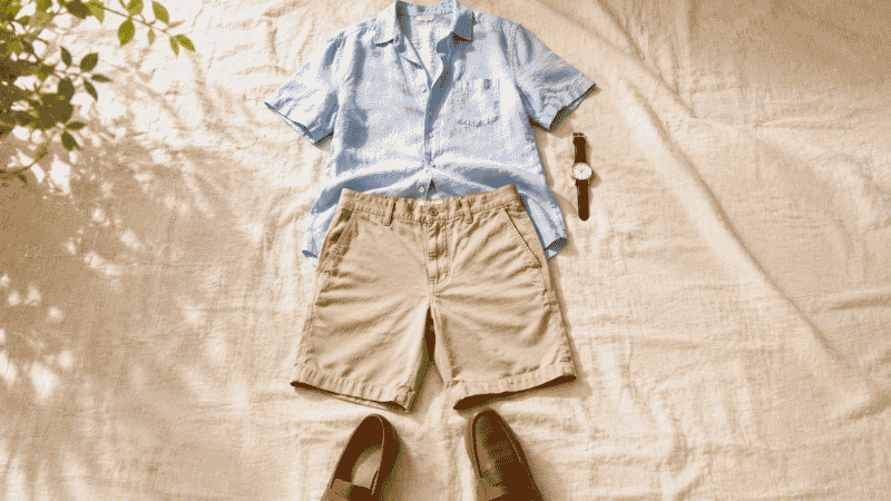 men's summer smart casual outfit flat lay with light blue linen short sleeve shirt khaki chino shorts and tan loafers