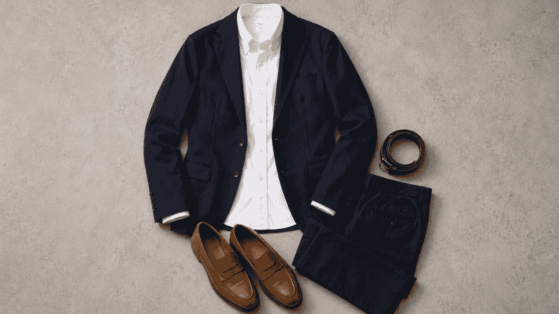 men's business casual interview outfit flat lay with navy unstructured blazer white oxford shirt dark chinos and tan leather loafers