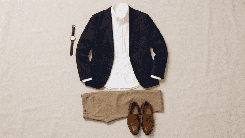 men's smart casual wedding guest outfit flat lay with navy unstructured blazer white oxford shirt khaki chinos and tan leather loafers