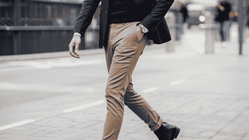 A well-fitted man wearing slim-tapered British khaki chinos paired with a navy blue blazer and dark brown leather Chelsea boots for a smart-casual business look