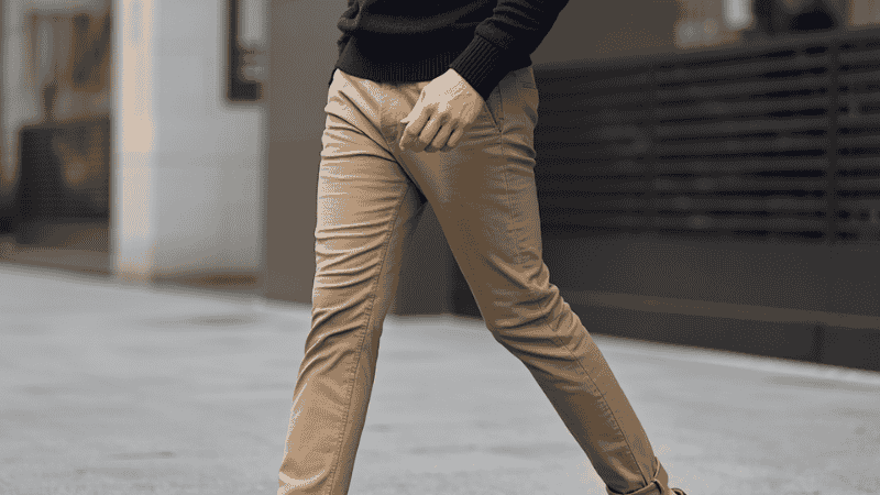 Full-body street style of a man wearing expertly tapered khaki chinos, a tucked-in navy crewneck sweater, and dark brown suede loafers, demonstrating proper pant length and color contrast