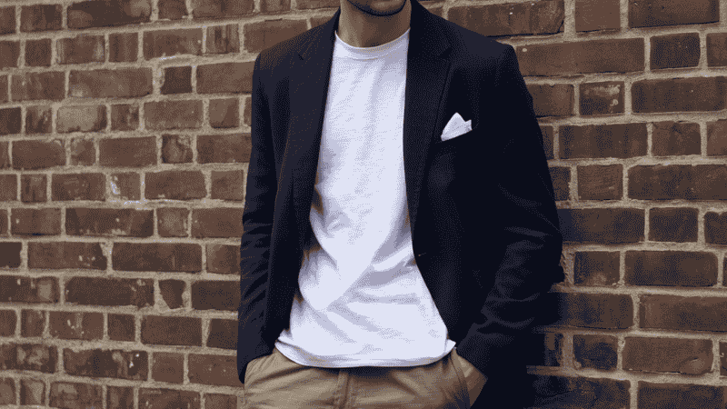 A man in a modern smart-casual outfit wearing an unstructured navy blazer over a clean white t-shirt and olive green chinos, showcasing a relaxed but professional silhouette.